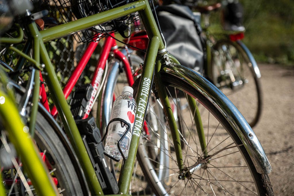 빨간색 자전거 옆에 'CYCLE CITY TOURS' 라벨이 붙은 녹색 자전거와 홀더에 든 물병을 클로즈업한 사진입니다.