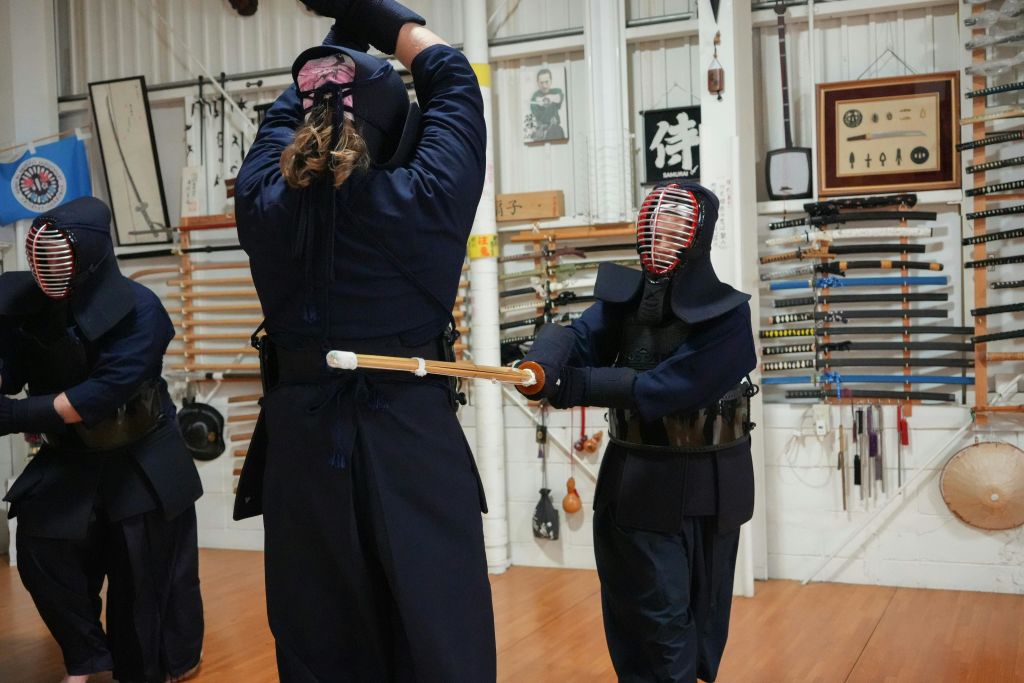벽에 각종 무기가 진열된 방에서 연습 중인 검도 장비를 입은 두 사람.