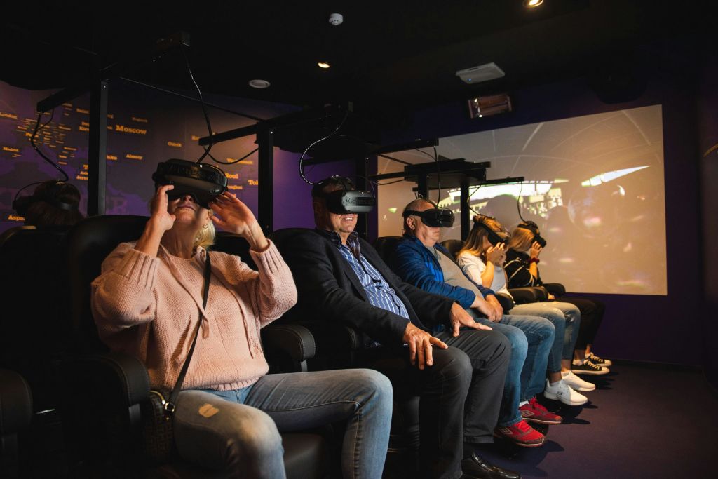 한 무리의 사람들이 어두운 방에서 가상 현실 헤드셋을 착용하고 나란히 앉아 공유된 VR 경험에 참여하고 있습니다.