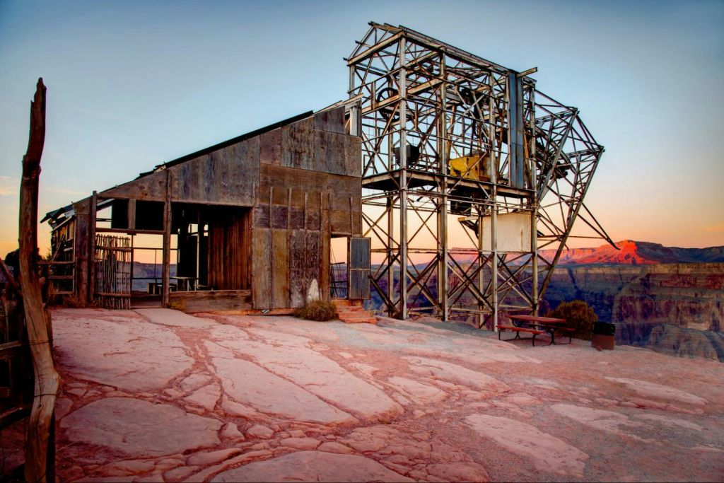 해질 무렵 경치 좋은 협곡을 배경으로 강철 프레임워크가 있는 소박한 목조 및 금속 구조물.