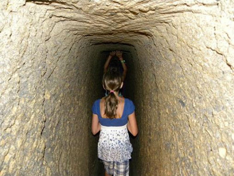 두 명의 어린이가 좁고 바위 벽으로 둘러싸인 터널을 지나고, 한 명의 어린이가 천장에 닿기 위해 손을 뻗습니다.