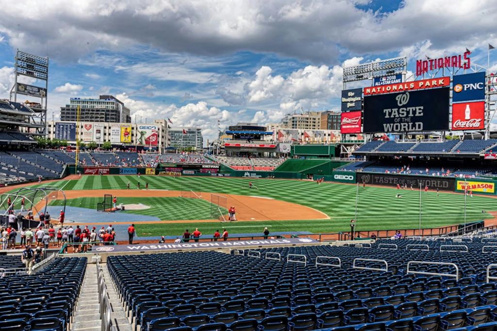 비어 있는 좌석 공간과 부분적으로 흐린 하늘 아래에서 운동장에서 연습하는 선수들이 있는 야구 경기장입니다.