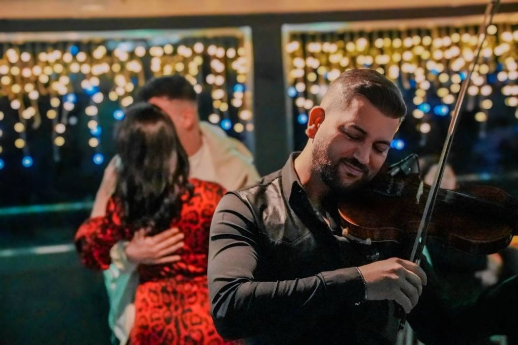 한 남성이 배경에 흐릿한 장식 조명이 켜진 따뜻한 분위기에서 열정적으로 바이올린을 연주하고 있습니다.