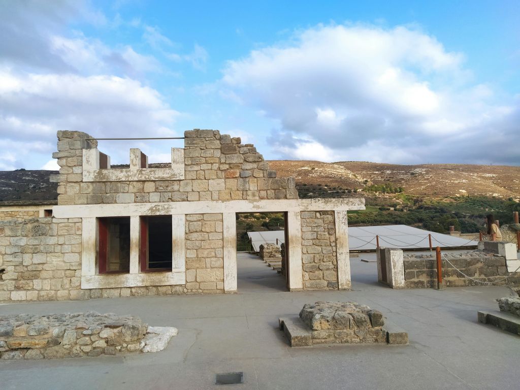 언덕을 배경으로 일부 흐린 하늘 아래 고대 석조 건물이 있으며, 근처에 현대적인 건축물이 있습니다.