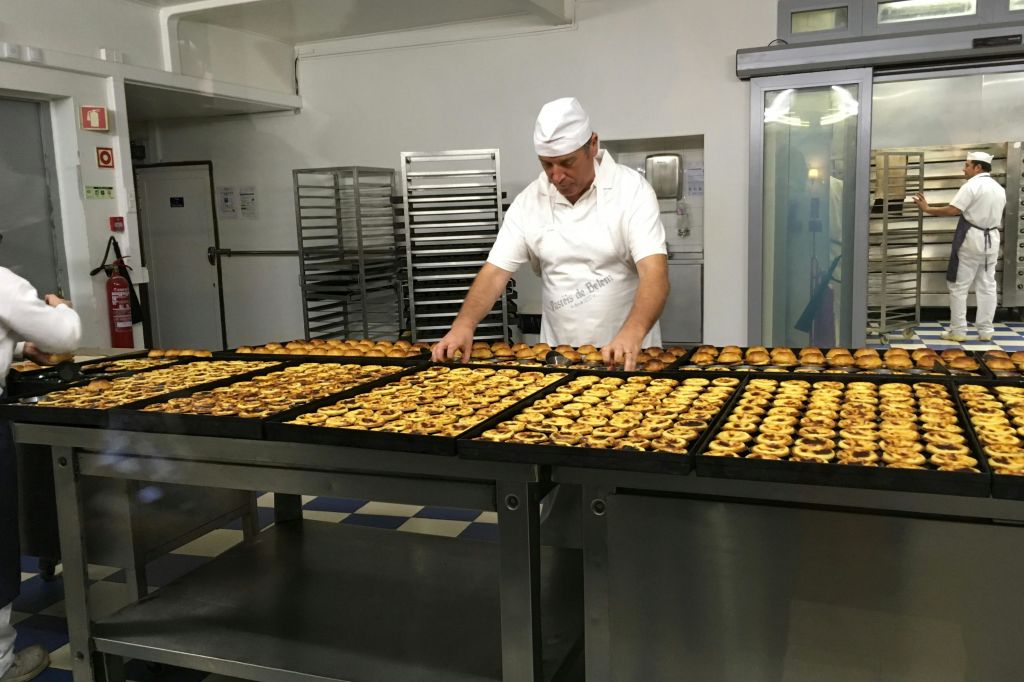 흰색 유니폼을 입은 제빵사가 상업용 주방의 커다란 테이블에 패스트리 트레이를 배치합니다.