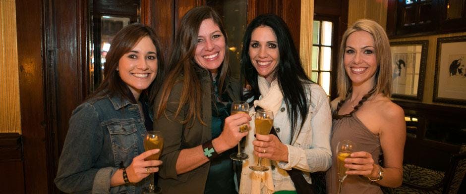 잔을 들고 음료를 마시며 웃고 있는 두 여성이 나무 패널을 배경으로 따뜻한 분위기를 자아내고 있습니다.