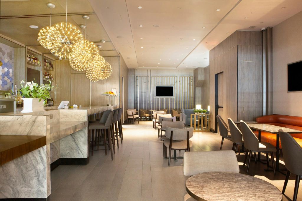 원형 테이블, 쿠션이 있는 의자, 높은 스툴이 있는 바, 장식용 행잉 조명이 있는 현대적인 라운지. TV가 뒷벽에 장착되어 있습니다.