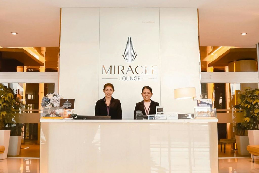 현대적이고 조명이 밝은 인테리어 디자인을 배경으로 두 명의 리셉션 직원이 미라클 라운지 프런트 데스크에 서 있습니다.