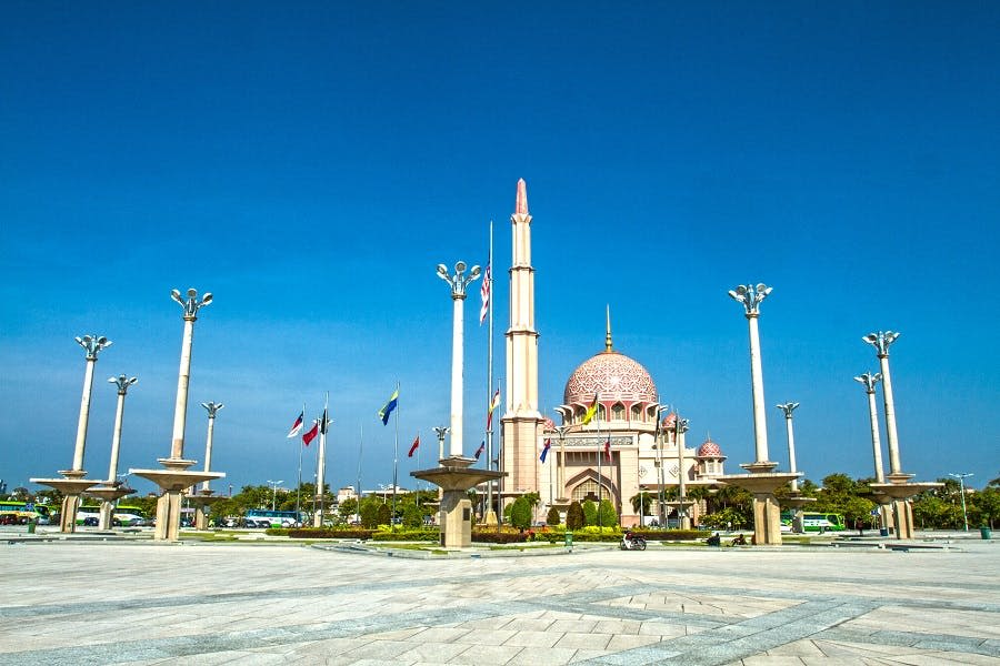 청명한 푸른 하늘 아래 깃발과 전등 기둥으로 둘러싸인 높은 첨탑이 있는 화려한 분홍색 돔 모스크.