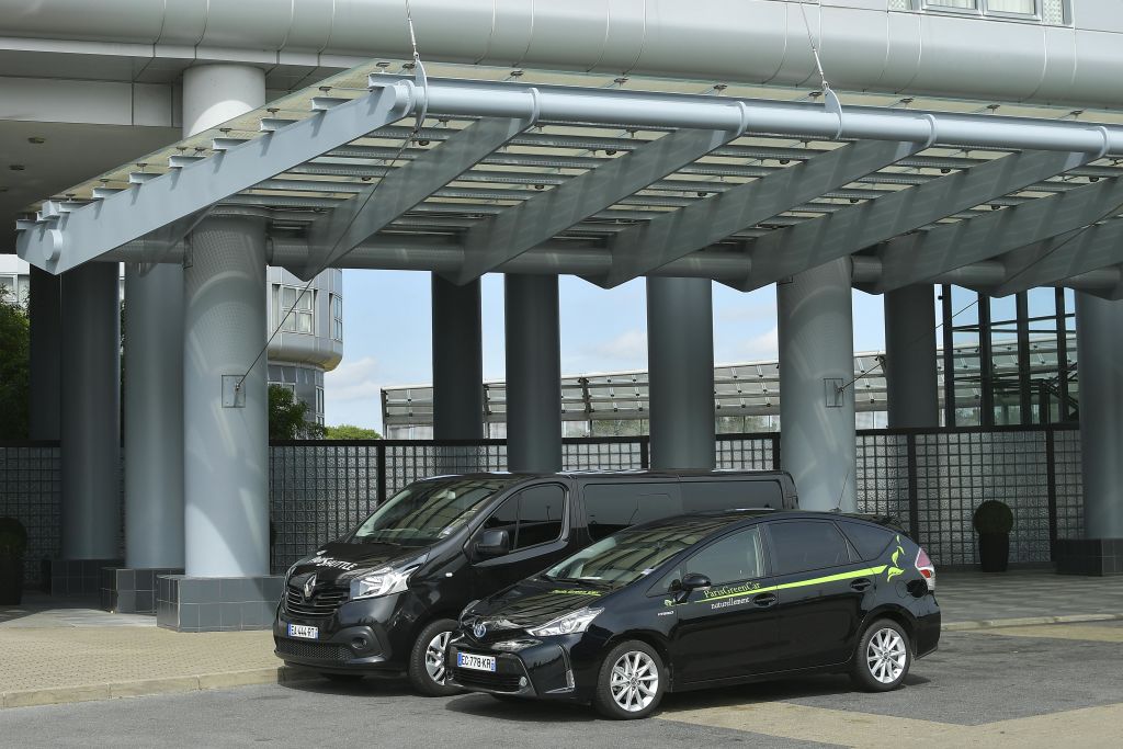 두 대의 검은색 자동차, 한 대의 밴, 한 대의 세단이 인더스트리얼 요소를 배경으로 금속 캐노피 구조 아래에 주차되어 있습니다.