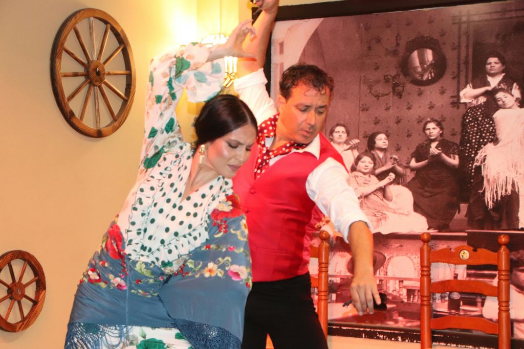 스페인 전통 복장을 한 남성과 여성이 비슷한 장면의 대형 흑백 사진 앞에서 플라멩코 춤을 추고 있습니다.