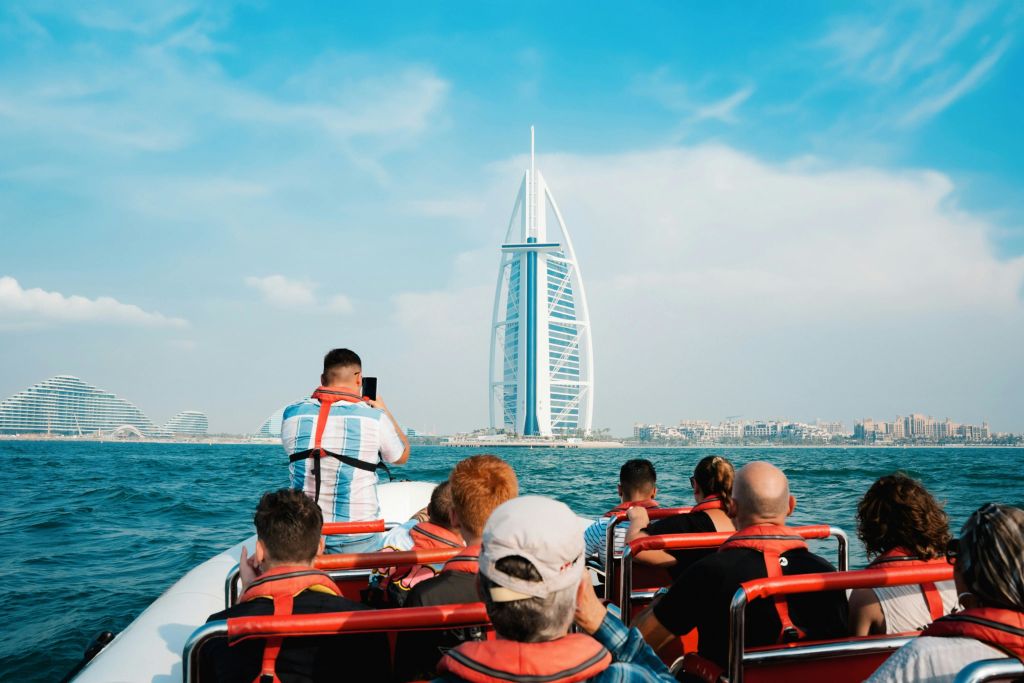 맑은 날 바다에서 돛단배 모양의 호텔인 부르즈 알 아랍 (Burj Al Arab) 의 사진을 찍는 보트를 탄 사람들.