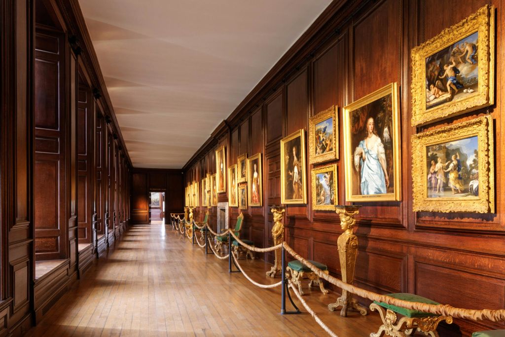 액자에 담긴 그림, 화려한 벤치, 밧줄이 달린 산책로가 있는 나무 패널이 있는 긴 갤러리입니다.