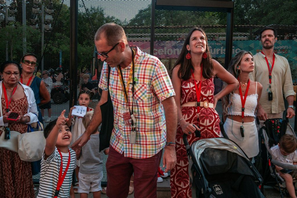 한 가족이 야외에 함께 서 있습니다. 체크무늬 셔츠를 입은 남성, 빨간색 드레스를 입은 여성, 줄무늬 셔츠와 유모차를 입은 소년.