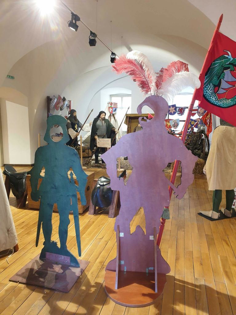 나이트 컷아웃, 깃털 깃털, 붉은 용 깃발을 배경으로 한 중세 박물관 전시가 있습니다.