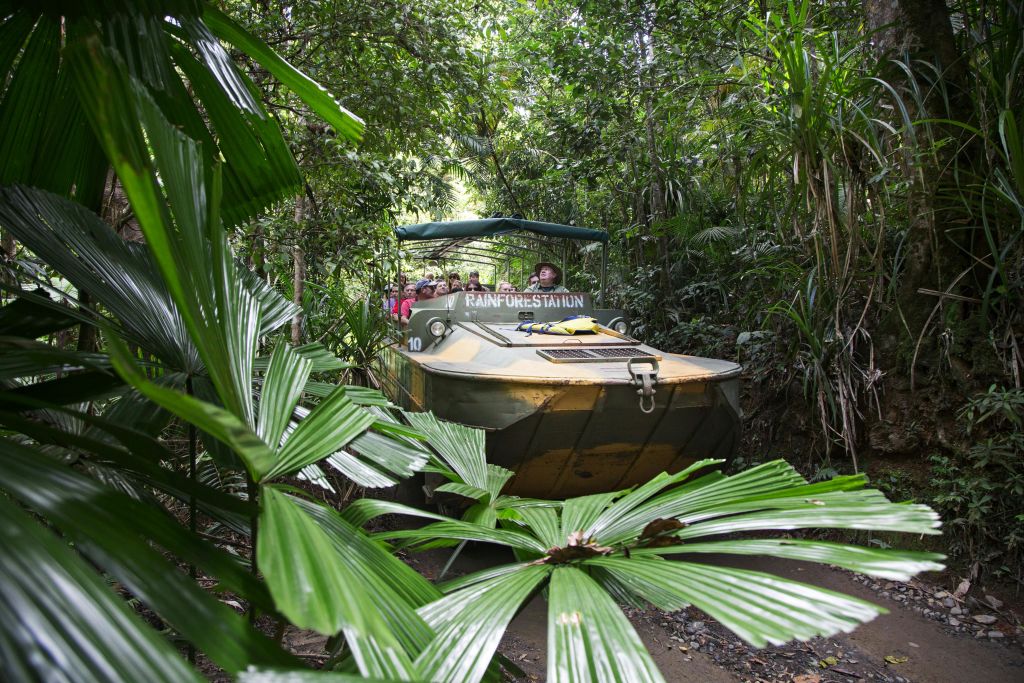 한 무리의 사람들이 "열대 우림" 이라는 이름의 수륙 양용 차량을 타고 빽빽한 녹색 열대 우림을 지나고 있습니다.