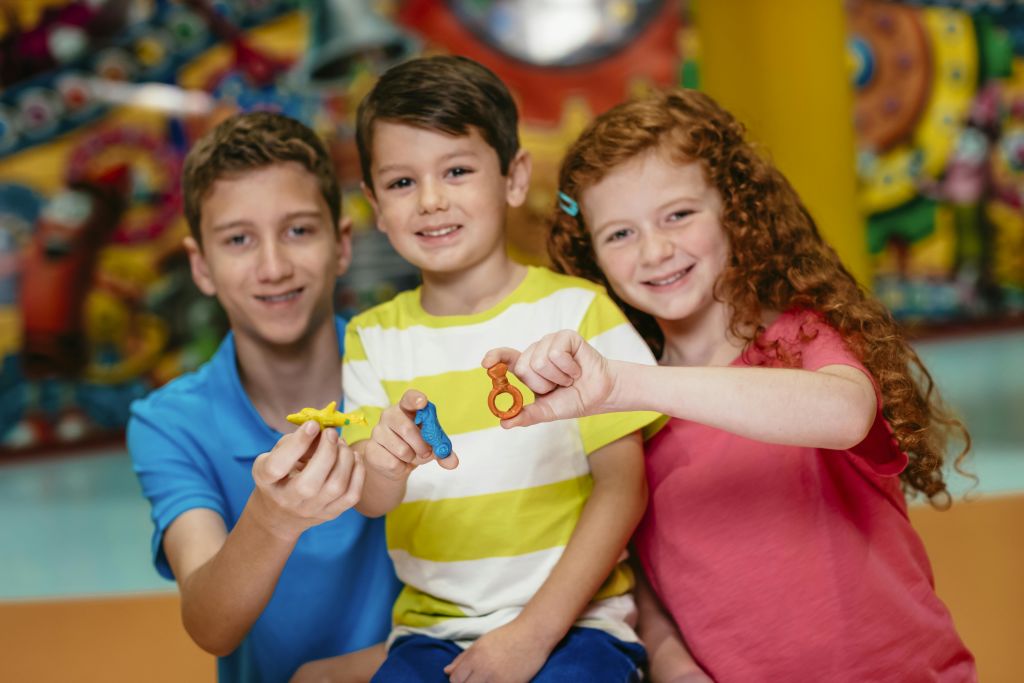 활기차고 흐릿한 배경과 함께 알록달록한 작은 장난감을 들고 웃고 있는 세 명의 어린이.