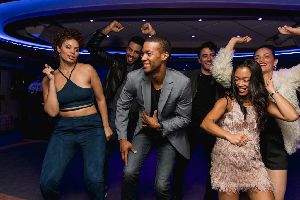 파란색 조명과 현대적인 천장이 있는 파티에서 한 무리의 사람들이 춤을 추며 미소를 짓고 있습니다.