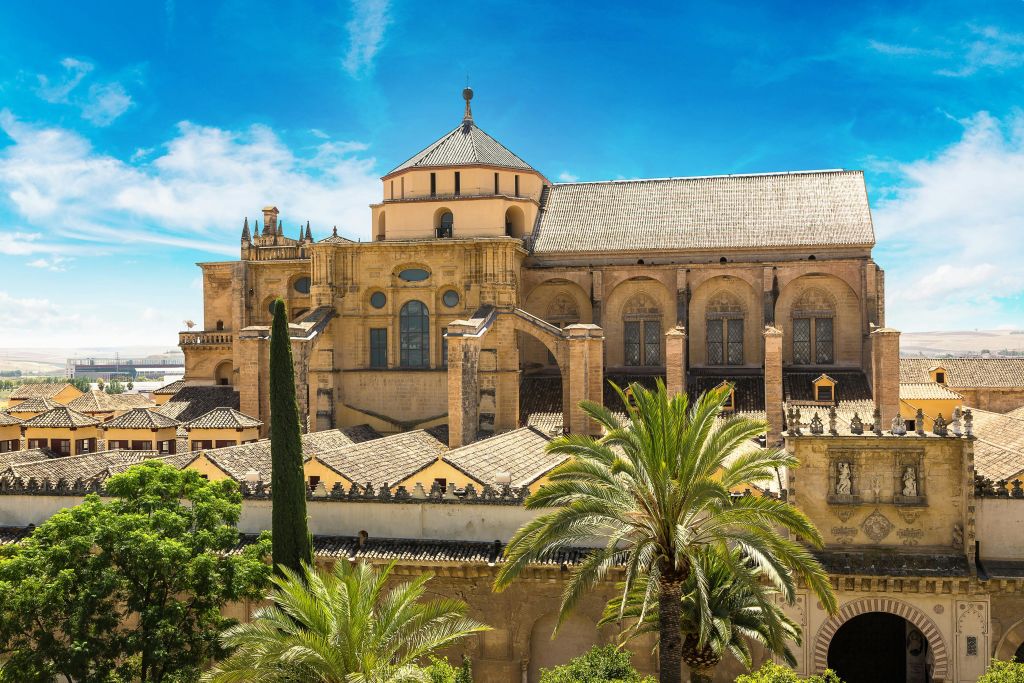 활기찬 푸른 하늘 아래 전경에 아치형 창문, 돔, 야자수가 있는 유서 깊은 석조 건물.