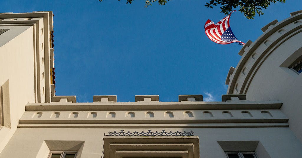 장식적인 장식이 돋보이는 건물 정면, 위로는 푸른 하늘, 오른쪽 상단에는 미국 국기가 흔들리고 있습니다.