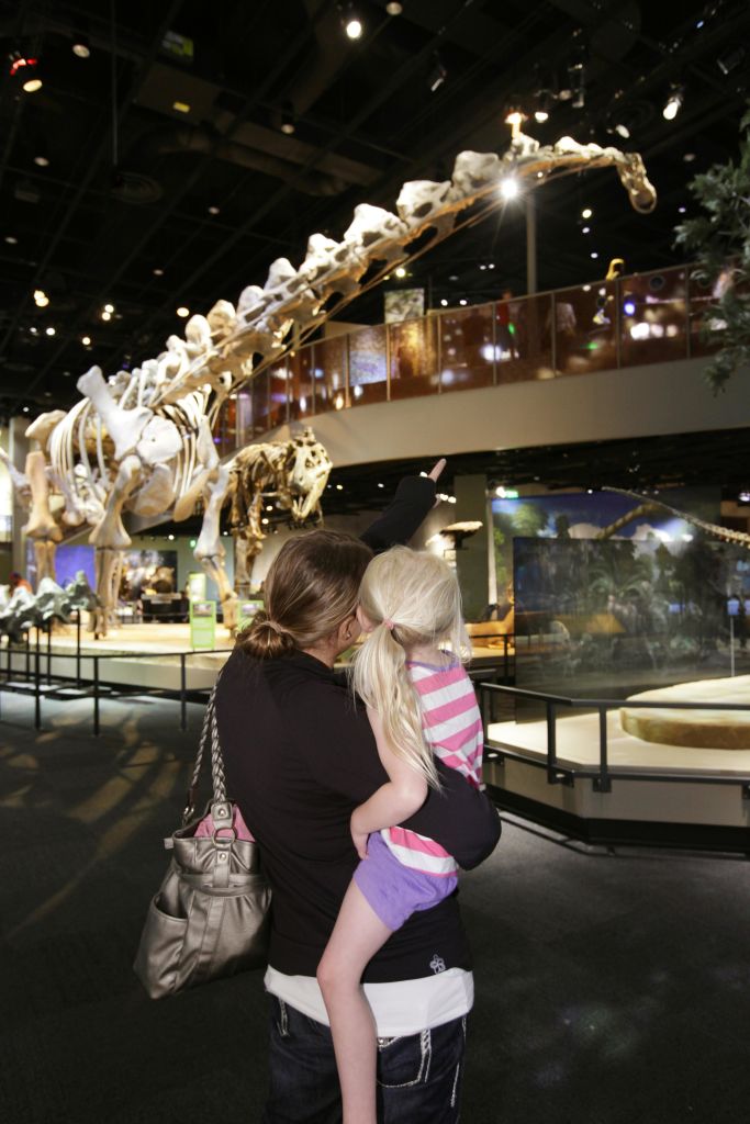 한 여성이 박물관 내부의 커다란 공룡 해골을 향해 아이를 안고 가리키고 있습니다.