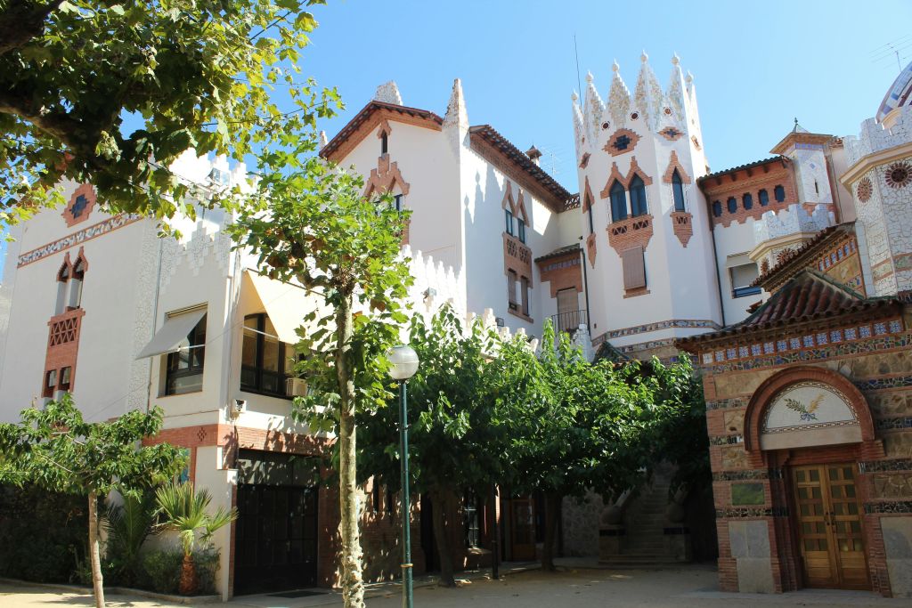 장식용 벽돌로 포인트를 준 흰색의 화려한 건물로, 울창한 나무로 둘러싸여 있으며 밝은 햇살로 조명을 받습니다.