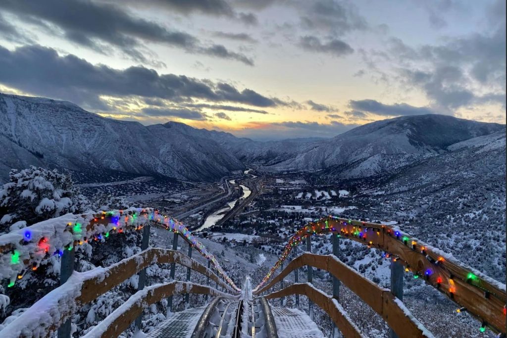 구불구불한 강이 흐르는 계곡으로 이어지는 화려한 조명으로 장식된 미끄럼틀이 있는 석양의 눈 덮인 산 풍경.