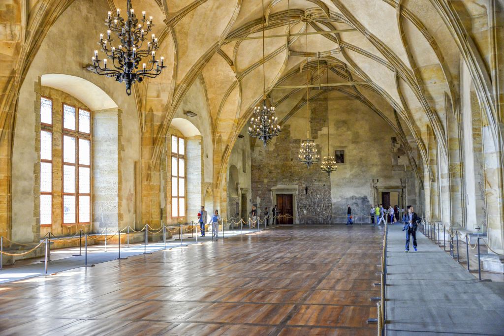 아치형 천장과 샹들리에, 커다란 창문이 있는 그랜드 홀입니다. 여러 사람이 로프를 따라 걷거나 서 있습니다.