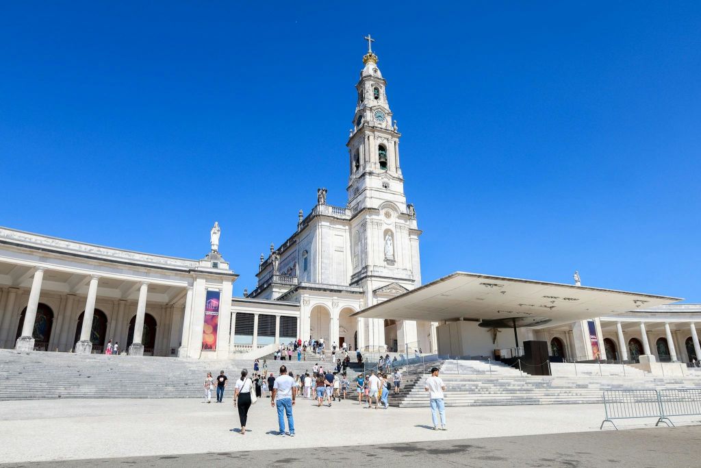 관광객들은 맑고 푸른 하늘 아래 높이 솟은 종탑이 있는 크고 화려한 교회 근처를 걸어갑니다. 입구까지 계단이 이어집니다.