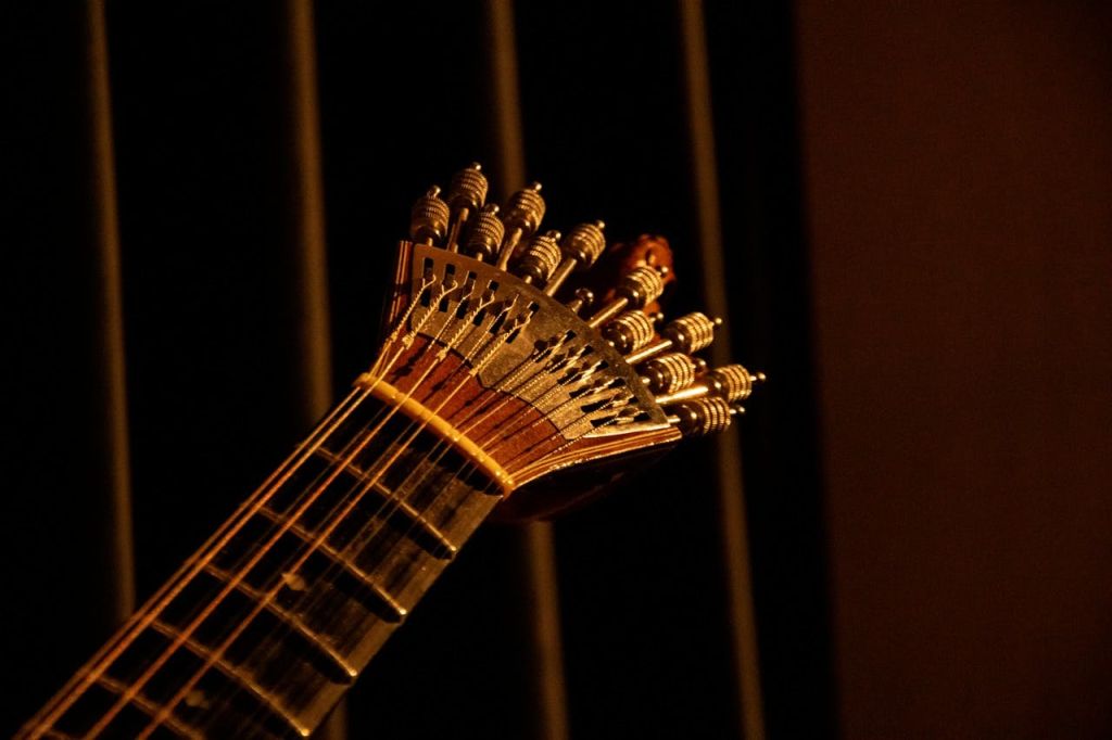 어두운 배경에 희미하게 불이 들어오는 튜닝 페그가 있는 멀티 스트링 악기의 헤드스톡을 클로즈업합니다.