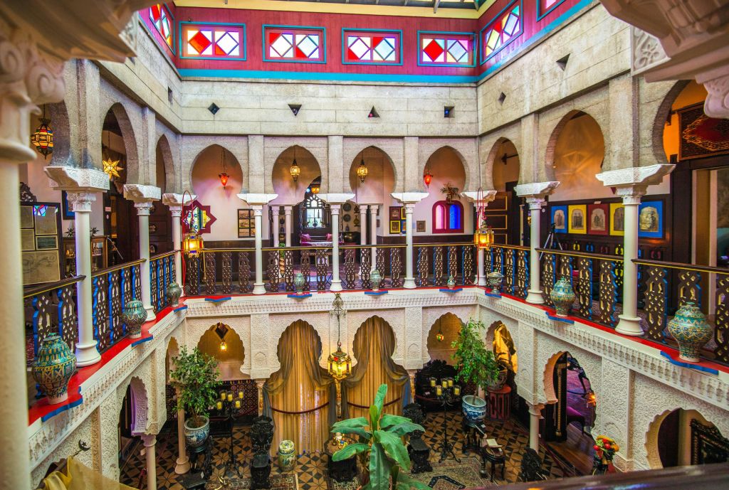 아치형 통로, 화려한 스테인드글라스, 화려한 난간, 매달린 등불, 화분이 있는 활기찬 복층 인테리어.