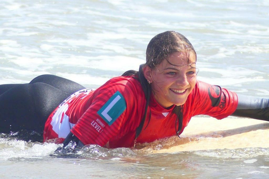 붉은 잠수복을 입은 사람이 얕은 바다에서 서핑 보드에 누워 미소를 짓고 있습니다.