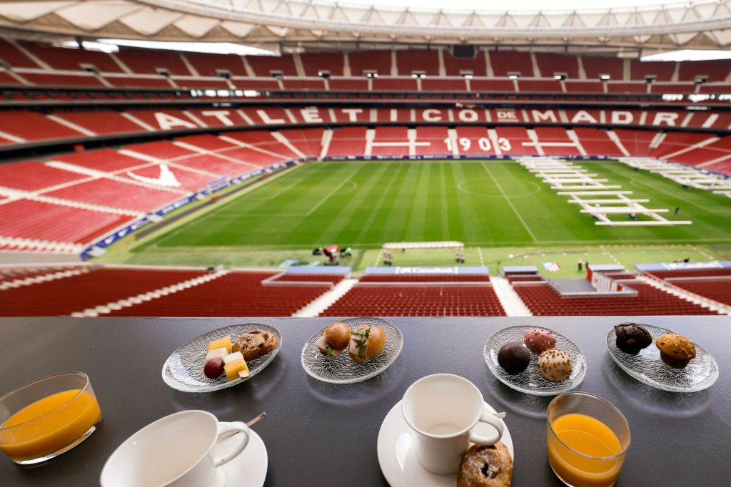 테이블 위에 작은 접시의 간식과 컵이 놓인 스위트룸에서 보이는 푸른 밭이 있는 축구 경기장의 전망.