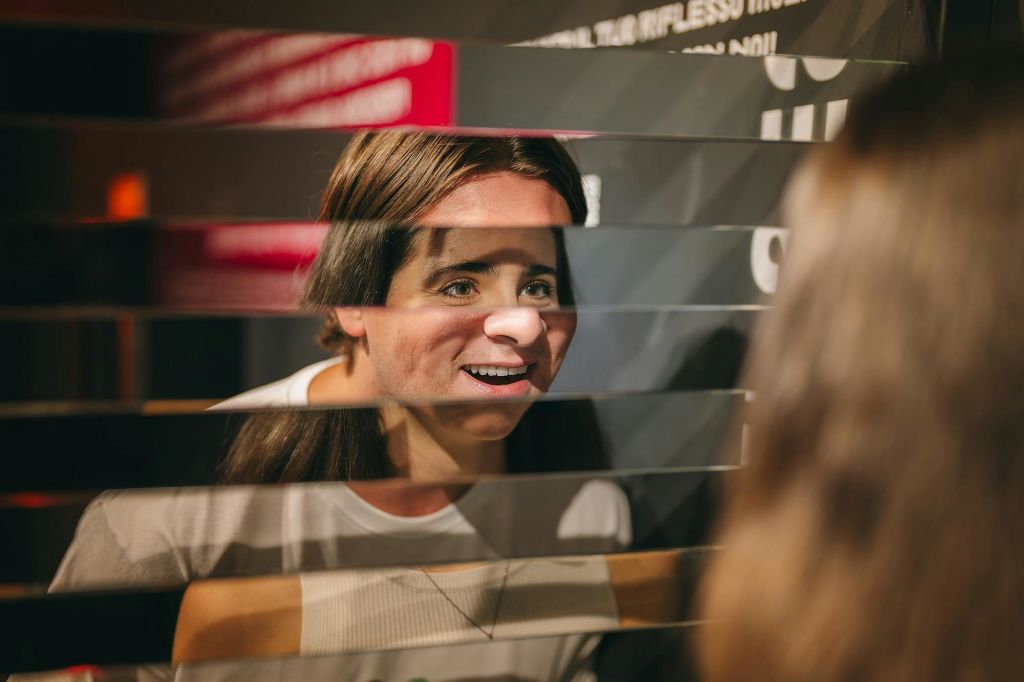 한 여성이 반사되고 슬롯이 있는 수평 유리 패널 뒤에서 미소를 지으며 조각난 시각 효과를 냅니다.