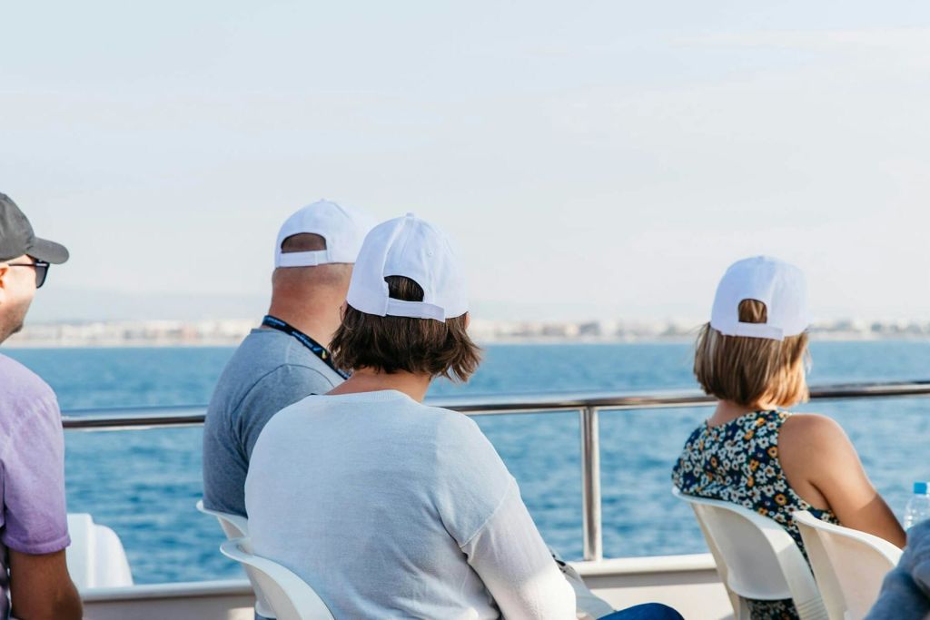 흰색 모자를 쓴 세 사람이 보트에 앉아 맑은 하늘 아래 바다를 마주하고 있습니다.