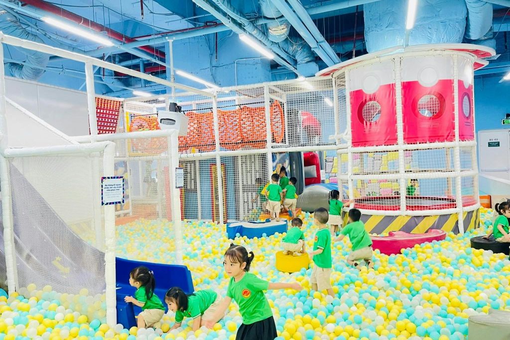 녹색 셔츠를 입은 아이들은 밝은 조명 아래에서 미끄럼틀과 등반 구조물이 있는 다채로운 실내 공 구덩이에서 놀고 있습니다.