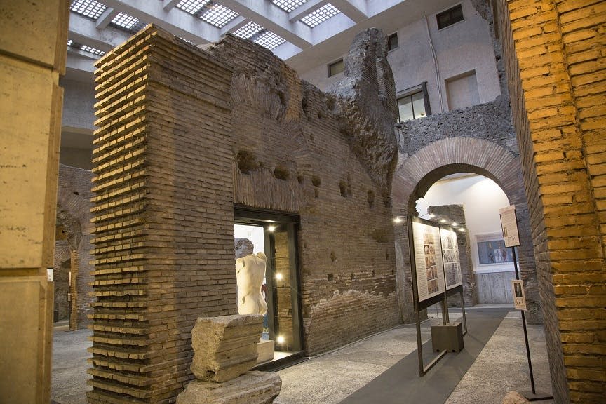 고대 벽돌 벽, 흰색 동상, 천장 천장 아래 정보 패널이 있는 현대적인 박물관 전시관입니다.