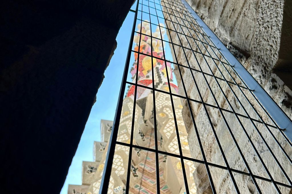 양쪽에 돌 벽이 있고 푸른 하늘 배경이 있는 블랙 메탈 그리드를 통해 화려하고 장식적인 타워의 모습.