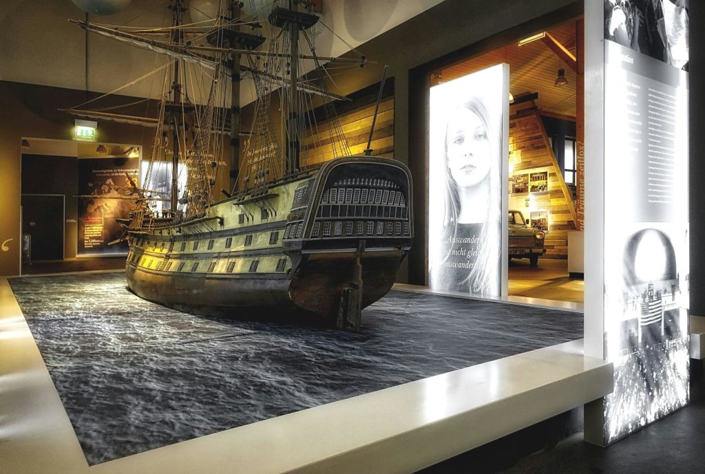 대형 선박 모델과 흑백 초상화를 포함한 조명 디스플레이 패널이 있는 박물관 내부.