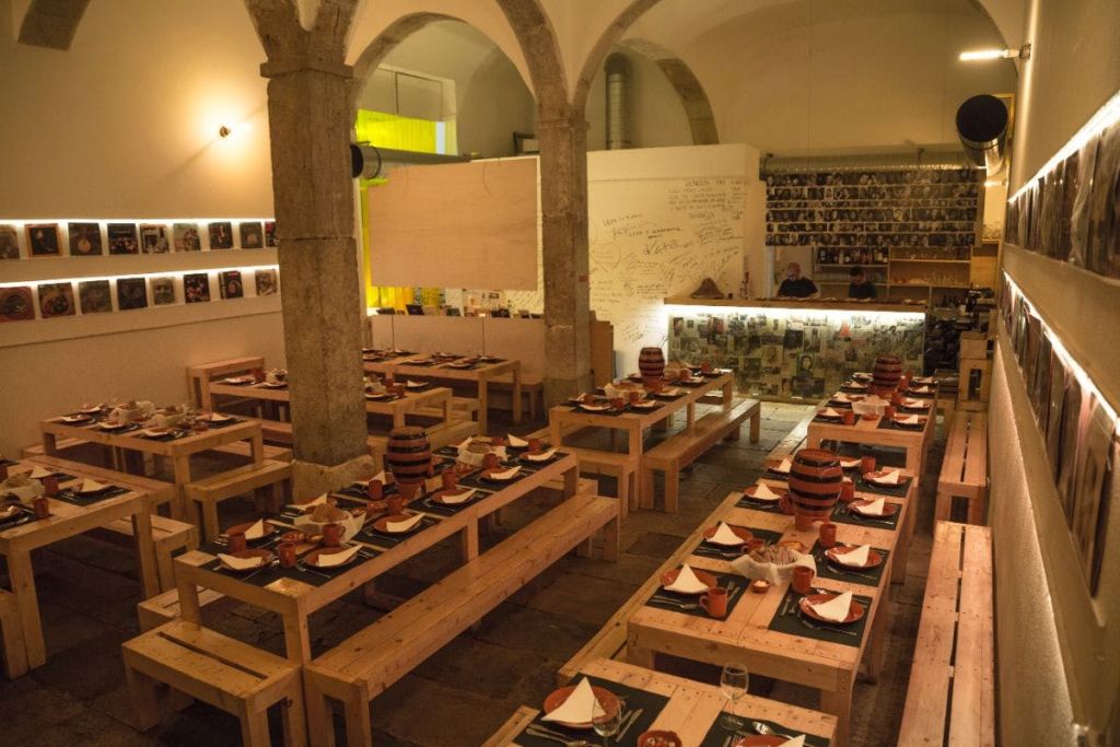 접시와 머그잔이 놓인 나무 테이블과 벤치가 있는 레스토랑입니다. 벽은 사진과 손으로 쓴 메시지로 장식되어 있습니다.