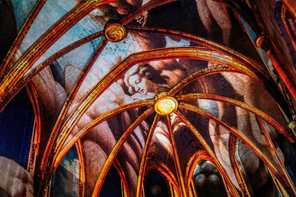 정교한 아치가 있는 대성당 천장과 커다란 페인트 천사의 모습이 따뜻한 조명으로 비춰집니다.