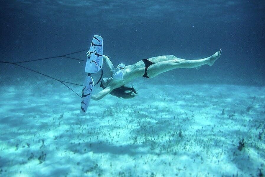 수영복을 입은 사람이 모래 바다 바닥을 배경으로 하얀색과 빨간색 카이트보드를 잡고 물속에서 헤엄치고 있습니다.