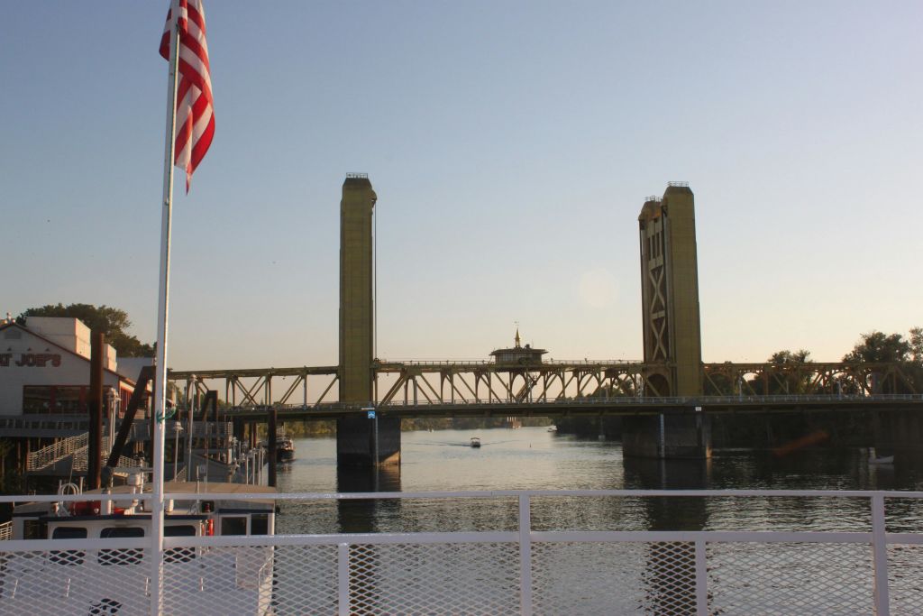 높은 탑이 있는 도개교는 석양이 지면 잔잔한 강을 가로지릅니다. 전경에 미국 국기가 보입니다.