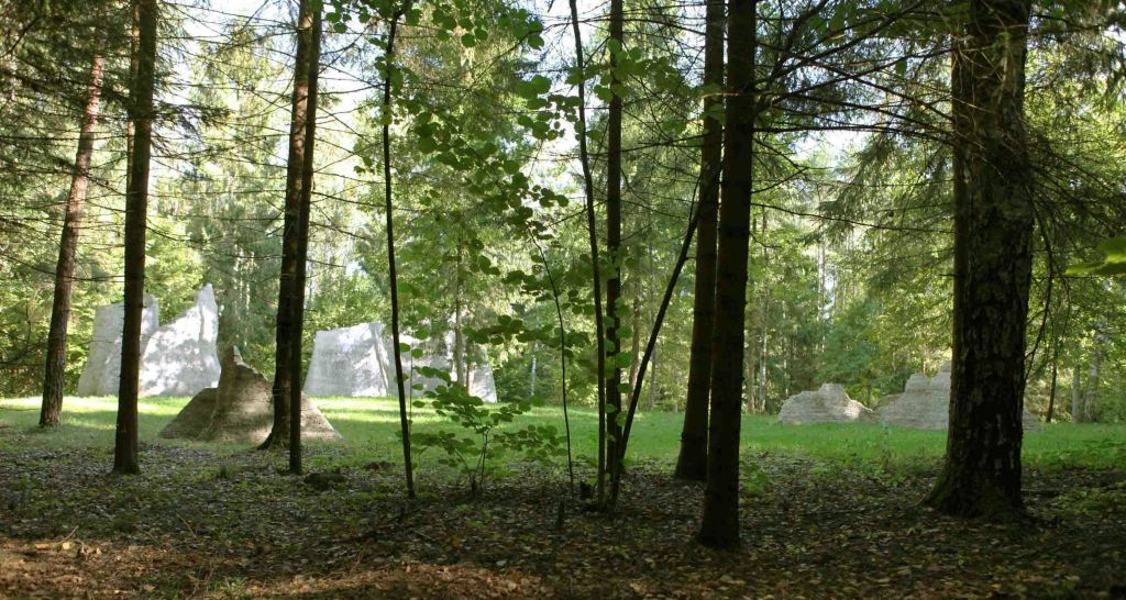 나무, 단풍을 거르는 햇빛, 커다란 바위 또는 구조물을 배경으로 한 숲 풍경.