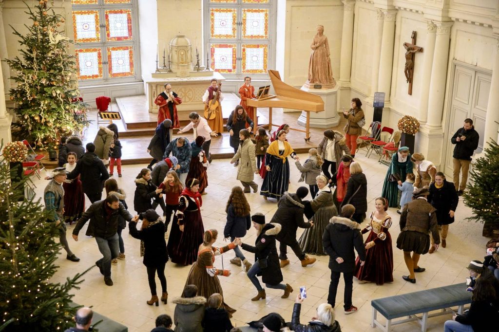 역사적인 의상과 현대적인 옷을 입은 사람들이 십자가와 스테인드글라스 창문이 있는 밝은 홀에서 춤을 추고 있습니다.