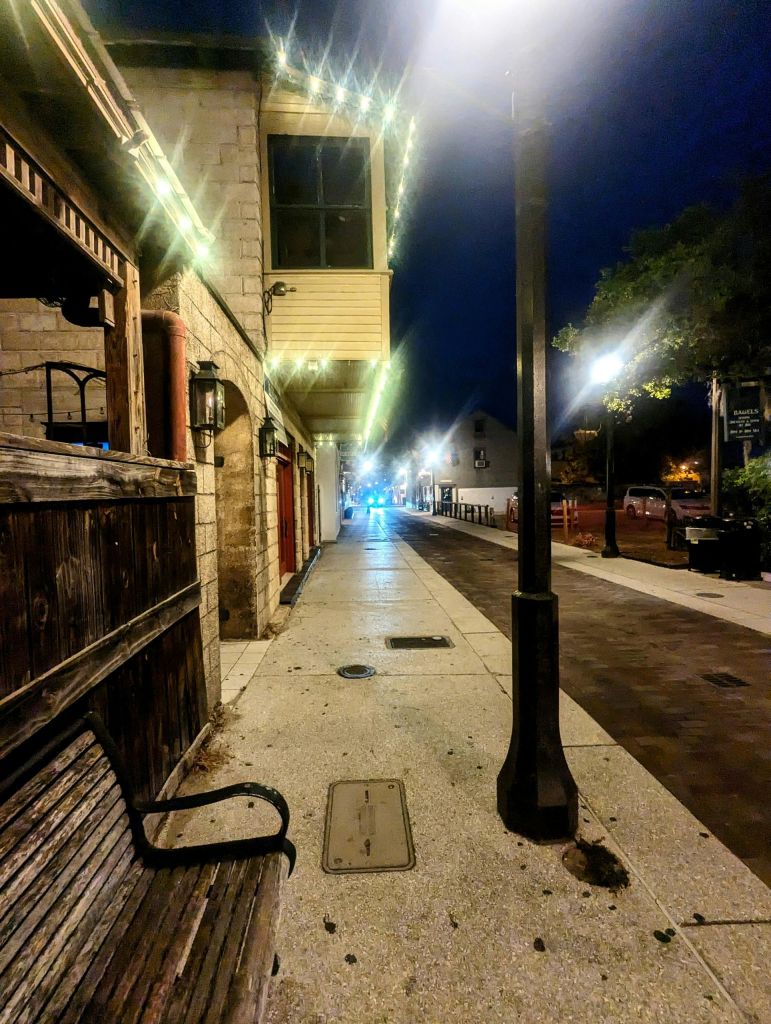 보도를 따라 벤치, 건물, 가로등이 있는 조용하고 조명이 밝은 밤의 도심 거리.