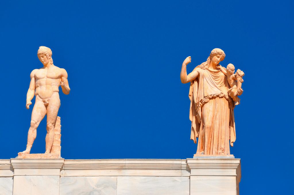 맑고 푸른 하늘을 배경으로 건물 지붕에 있는 두 개의 석상으로, 하나는 근육질 남성이고 다른 하나는 부분적으로 보이는 인물입니다.