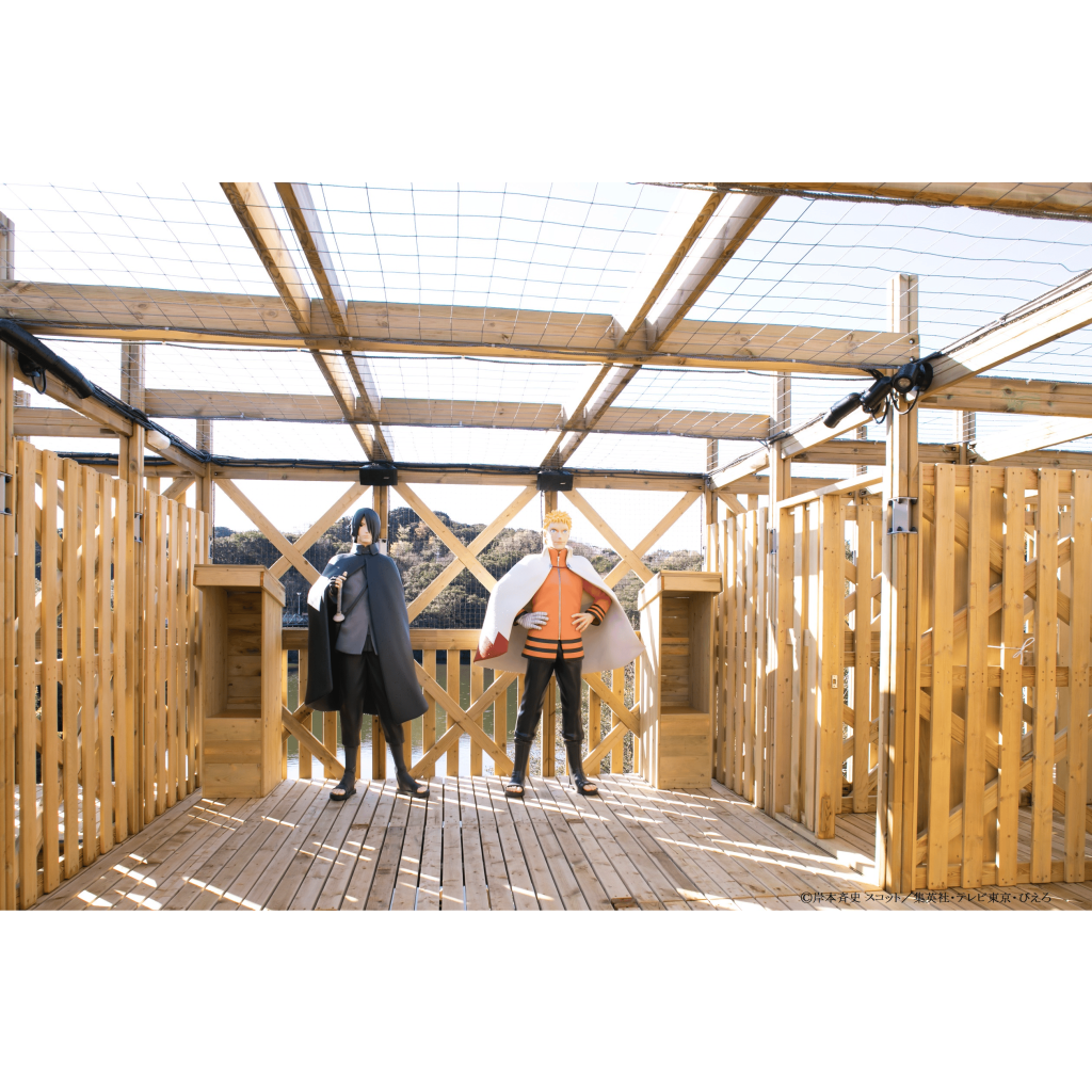 망토를 두른 두 마네킹과 머리띠가 그물 지붕과 열린 측면이 있는 울타리가 있는 목조 구조로 서 있습니다.