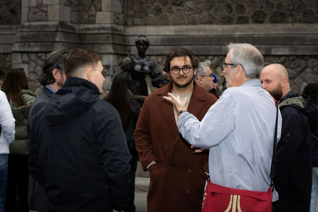 한 무리의 사람들이 석조 건물과 동상 근처의 야외 공간에서 대화를 나누고 있습니다.