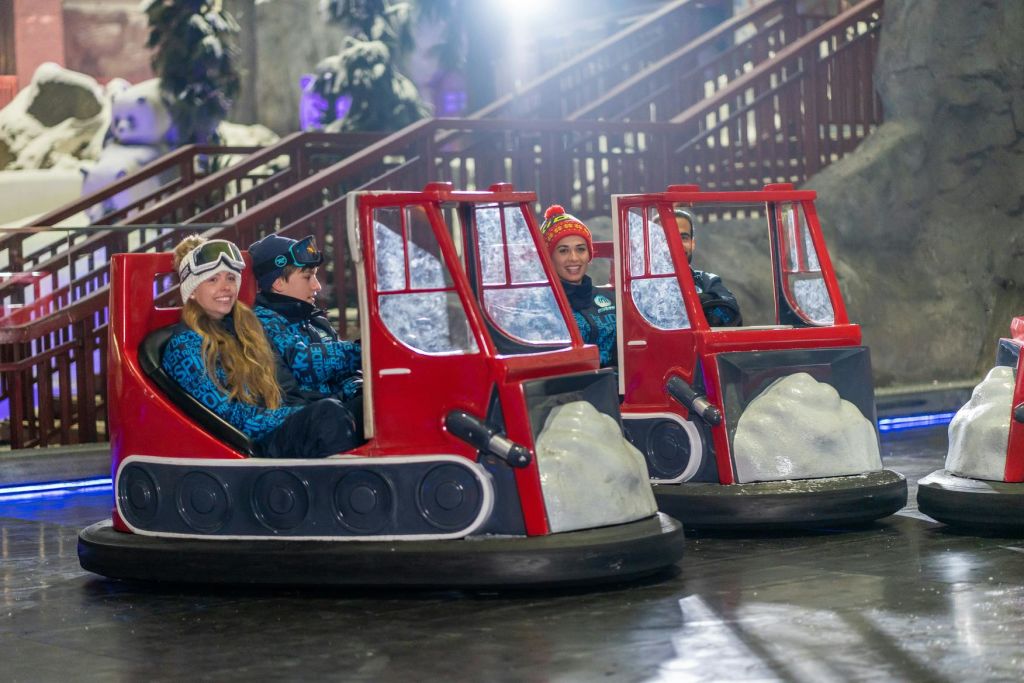 제설기 모양의 빨간 범퍼 자동차 두 대. 겨울 복장을 한 사람들이 미소를 짓고 라이딩을 즐깁니다.